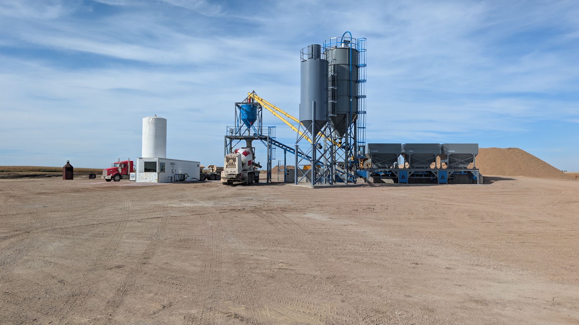 Mixer truck at the load hopper, with the plant and aggregate piles behind it.